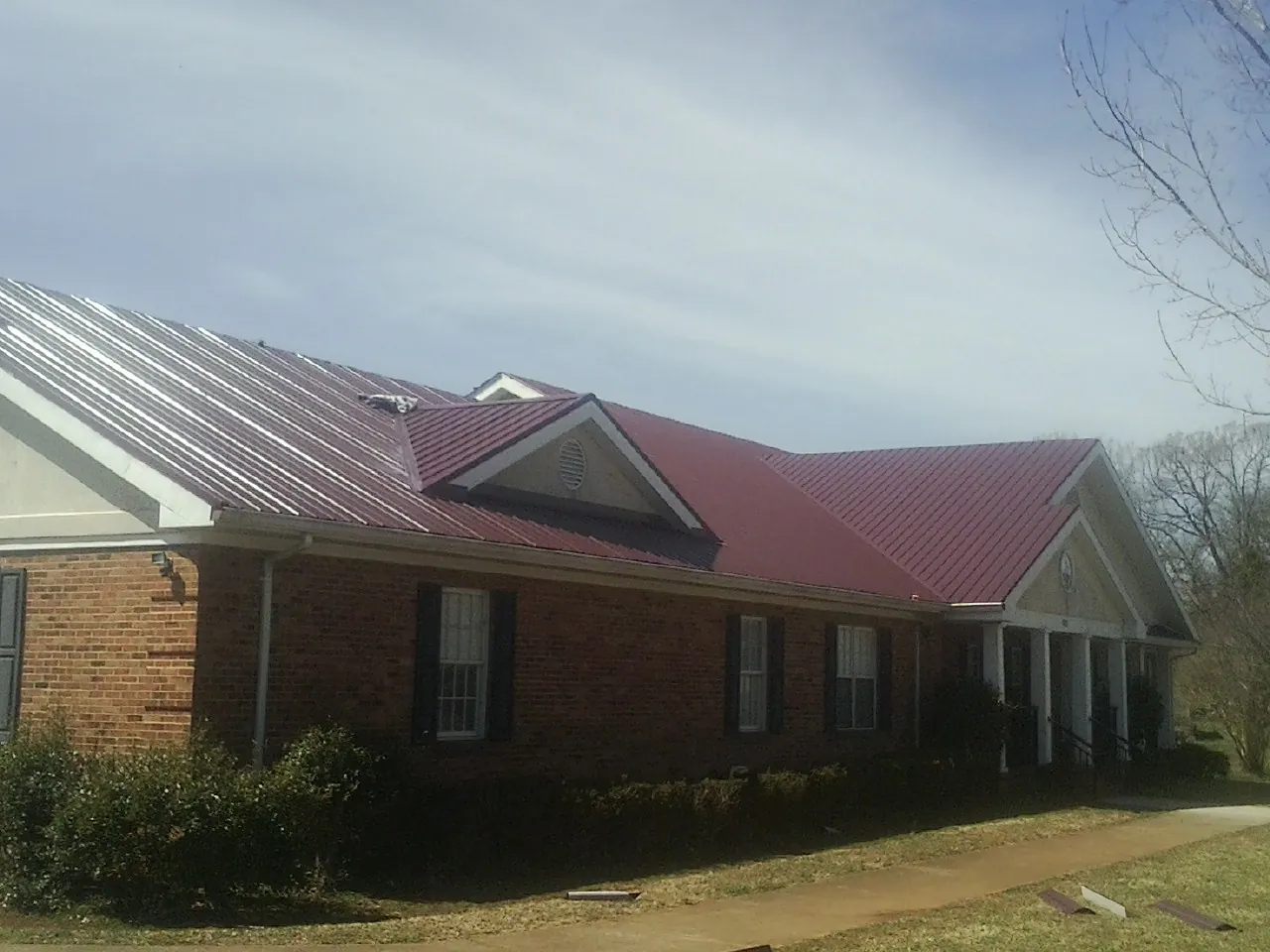 Red metal roof with gabled entries on a long brick building, from a Hail Damage Roof Repair job in Philipsburg