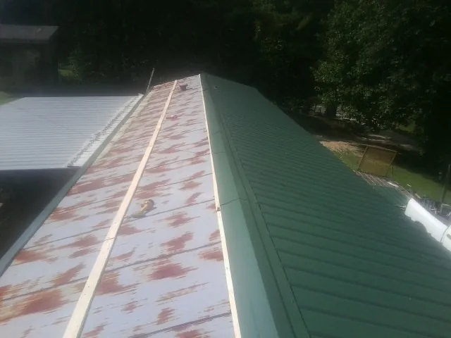 Old rusted panels beside newly installed green metal roofing — Wind Damage Roof Repair by Roofing Brothers in Philipsburg