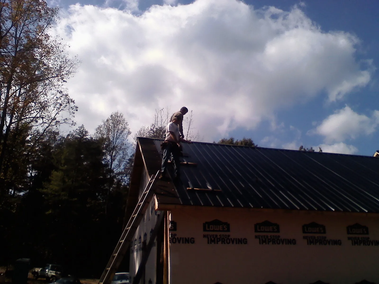 Roofer fastening dark metal panels high against a cloudy sky, from a Roof Inspection job in Philipsburg