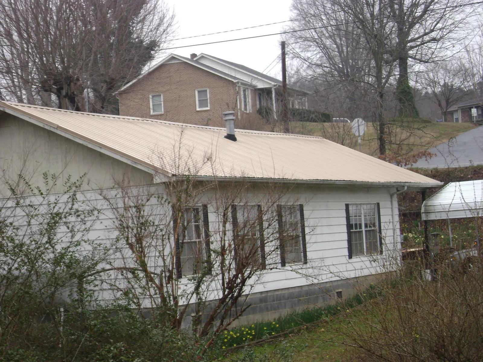 Tan metal roof on a white sided house set into a hillside — Commercial Roofing by Roofing Brothers in Philipsburg